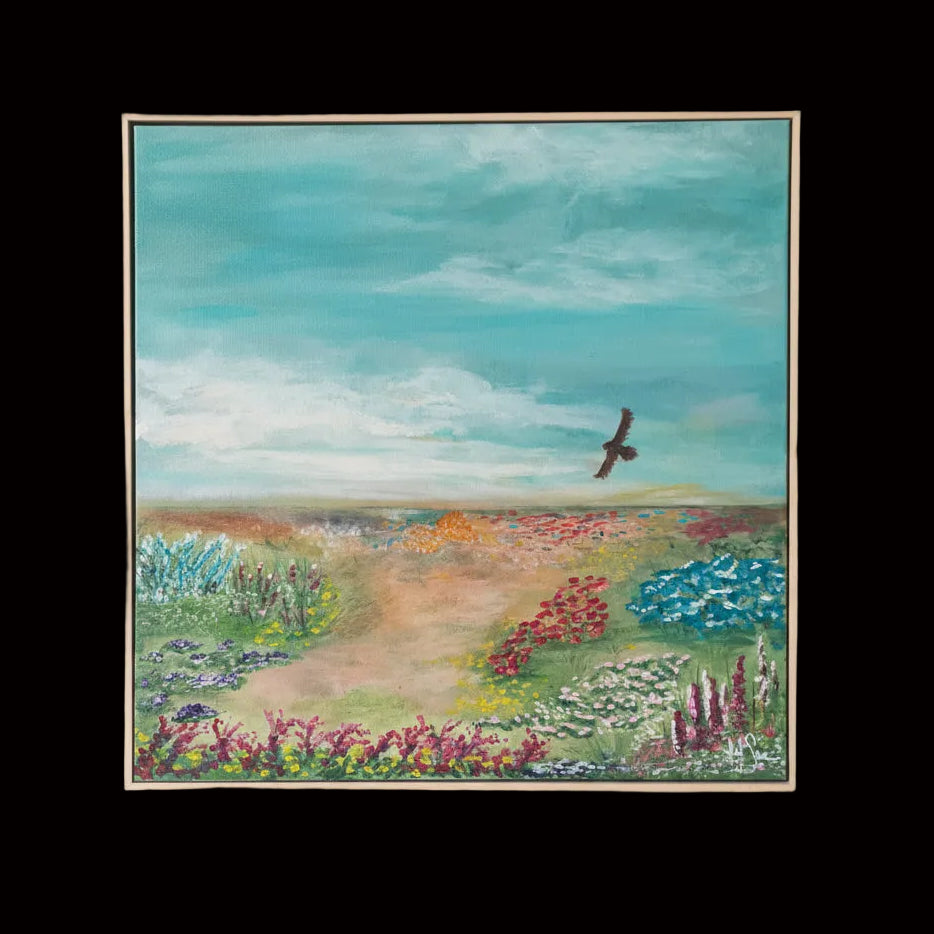 A square framed landscape painting featuring a winding dirt path through a colorful field of flowers under a teal-blue sky with a small bird in flight, displayed on a plain wall.
